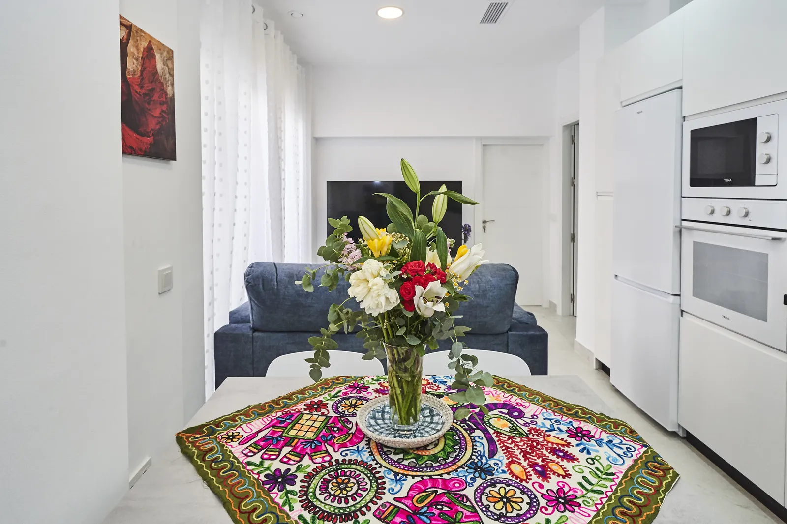 Salón con sofá azul, mesa de comedor y cocina al fondo en Casa Isolde